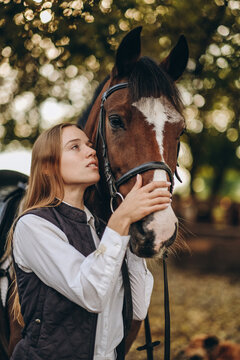 A young female equestrian stands near her horse and prepares for a competition.