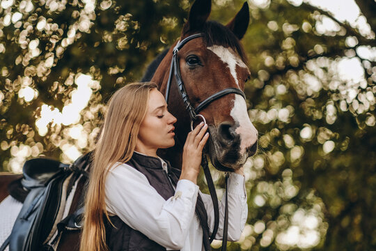 A young female equestrian stands near her horse and prepares for a competition.