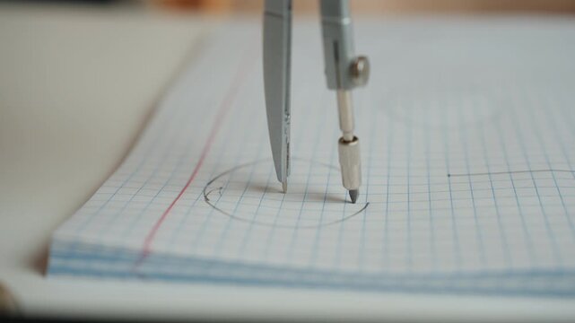 Compass drawing circle on notebook near red margin, focused homework practice at desk, closeup metal instrument carving arc on grid paper, determined student preparing for exam in quiet study setting.
