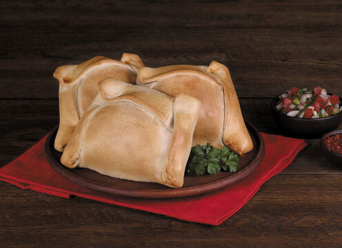 Traditional Chilean empanadas de pino with pebre sauce on rustic wooden table