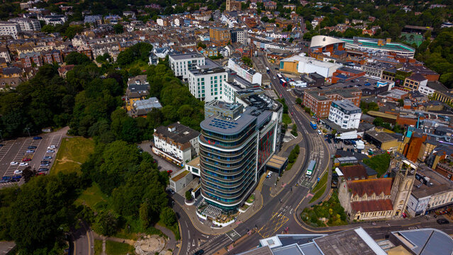 Aerial view of a modern curved building in the city center surrounded by urban streets, lush trees, and historic architecture in Bournemouth, England, United Kingdom.