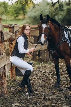 A young female equestrian stands near her horse and prepares for a competition.