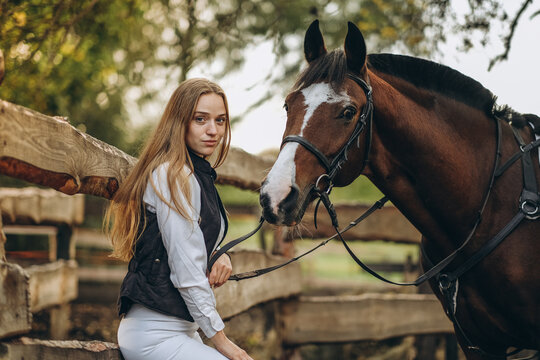 A young female equestrian stands near her horse and prepares for a competition.