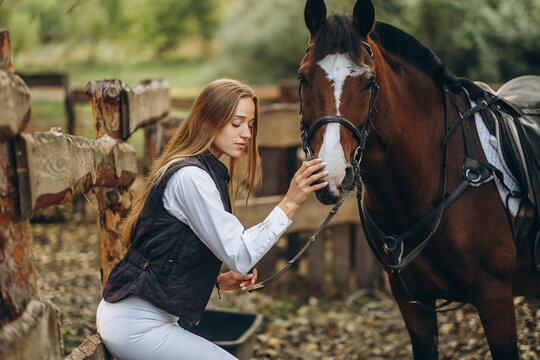 A young female equestrian stands near her horse and prepares for a competition.