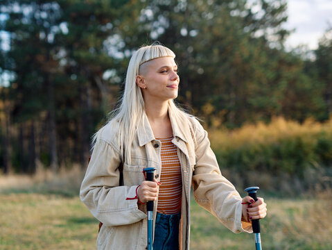 Hiking woman enjoys nature with trekking poles in a lush forest during a sunny day