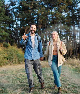 Hiking couple, young man and woman enjoys nature with trekking poles in a lush forest during a sunny day