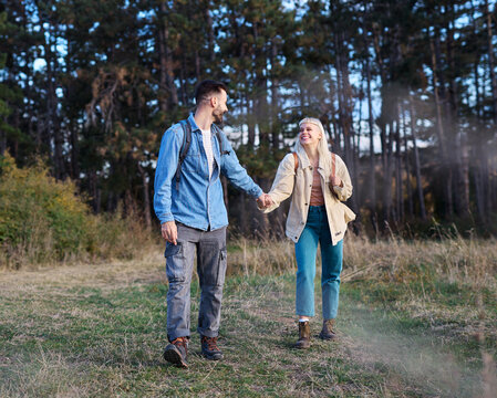 Hiking couple, young man and woman enjoys nature with trekking poles in a lush forest during a sunny day