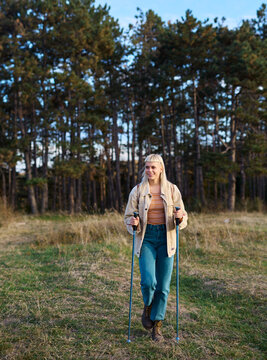 Hiking woman enjoys nature with trekking poles in a lush forest during a sunny day