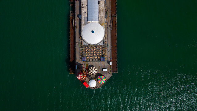 Aerial view of Bournemouth Pier with its white dome, outdoor seating, and colorful carousel rides extending into the dark green sea in Bournemouth, England, United Kingdom.