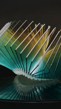 Vertical video: Opening acrylic fins on mirror, center lift starting ripple with teal-yellow light