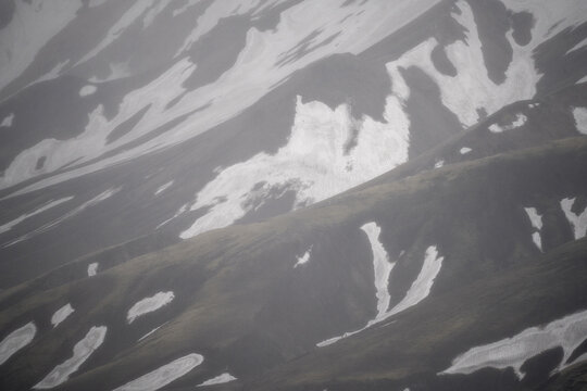 View of snow-covered mountain slopes with dark volcanic rock and patches of melting snow in Iceland.