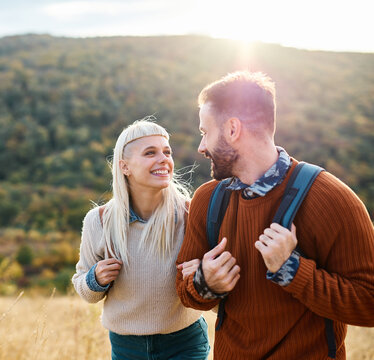 Hiking couple, young man and woman enjoys nature with trekking backpacks  in a lush forest during a sunny day