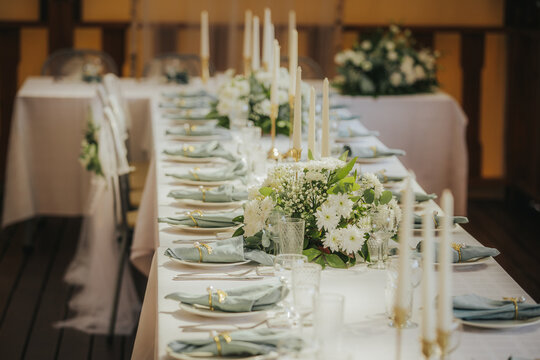 Elegant dining table set for a formal event with white flowers, candles, and neatly arranged plates and cutlery in a beautifully decorated indoor space