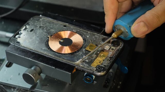 Smartphone repair in a service center, phone secured in a vise while technician removes old adhesive from the frame before installing replacement glass, phone parts and component replacement
