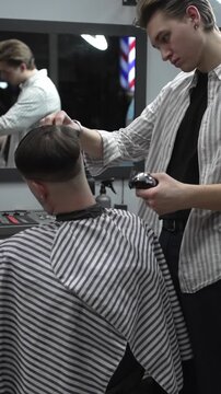 Professional barber grooming client's hair using electric clipper, delivering precise cut with skill in contemporary salon setting