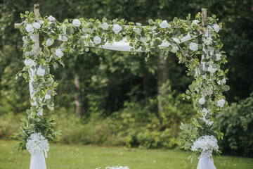Wedding arch adorned with white flowers and greenery set in a lush outdoor garden, creating a...