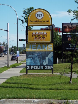 Gatineau, Quebec, Canada &ndash; June 24, 2026: A roadside sign advertising "Sp&eacute;cialiste SST" jeans for two for twenty-five dollars stands beside a street with traffic on Bd Gr&eacute;ber.