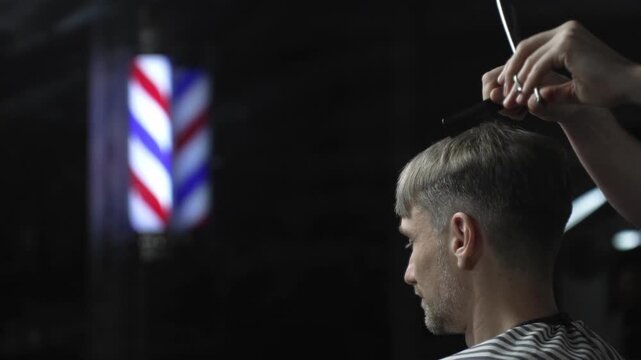 Professional barber grooming male client's hair with scissors, vintage barber pole framing traditional barbershop background