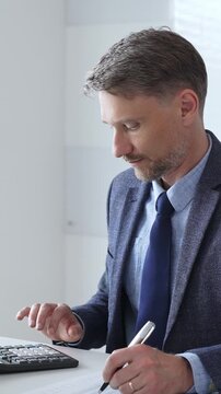 Focused businessman sitting at a modern desk, working intently on a laptop surrounded by folders, showcasing professionalism and determination. Audit and taxes in business