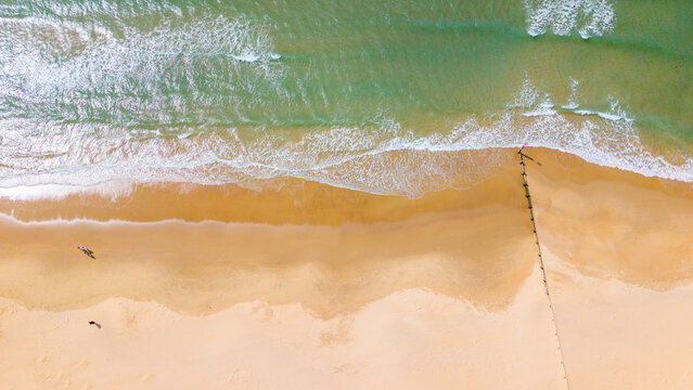 Aerial view of Bournemouth Beach with golden sand, turquoise waves, and a wooden groyne extending into the sea in Bournemouth, England, United Kingdom.