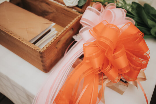 Orange and pink decorative ribbons arranged on a table beside a wooden box containing envelopes and flowers, creating an elegant gift presentation
