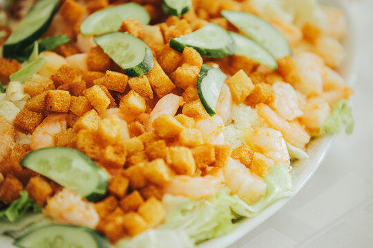 Fresh shrimp salad with lettuce, croutons, and cucumber slices arranged on a white plate, served on a light tablecloth in a dining setting