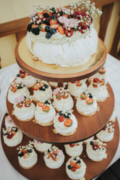 Multi-tiered dessert display featuring a large pavlova topped with fresh berries and flowers alongside individual pavlovas on a wooden stand