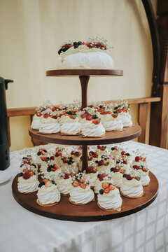 Three-tiered dessert display featuring meringue cakes topped with fresh berries and edible flowers on a wooden stand in a decorated indoor setting