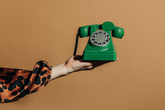 Hand hold green vintage rotary telephone on beige backdrop