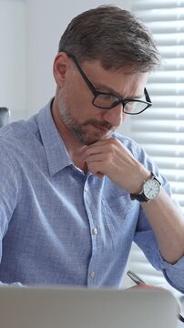 Businessman wearing blue sleek shirt is thinking and concentrating while working at the desk in a bright, modern office, demonstrating professionalism and efficiency. Business people concept