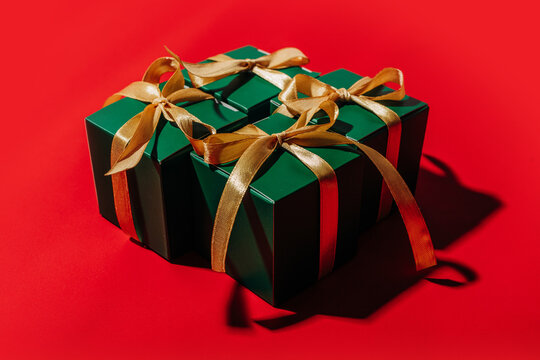 Green gift box with gold ribbon on bright red background