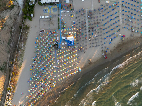 Aerial view of rows of sun umbrellas on the sandy beach with gentle waves of the Adriatic Sea in Porto San Giorgio, Marche, Italy.