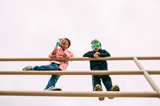 Two Young Children Wearing Costumes Playing on a Playground Climbing Structure