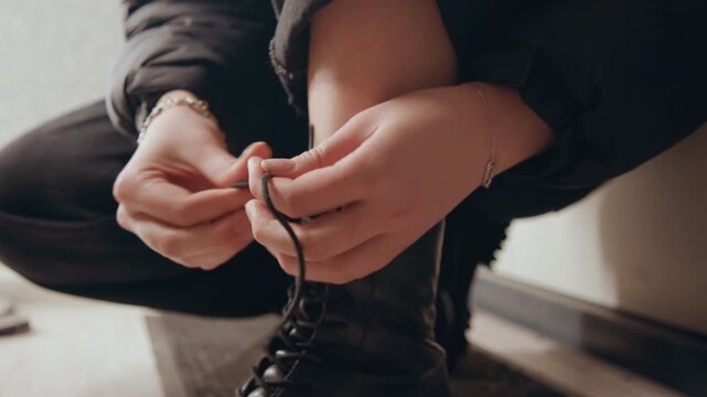 Closeup of boot lacing scene. Indoor scene with hands fastening black boot. Morning routine with hands tying leather boot on mat. Detailed view of hands securing boot laces in cozy indoor setting