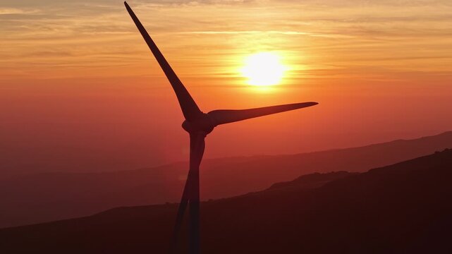 Wind turbine silhouette at dramatic orange sunset