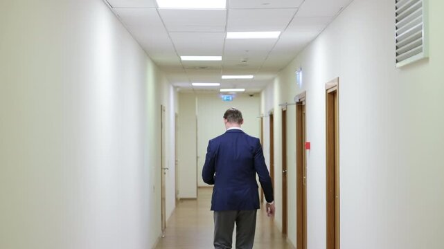 Successful male executive in a formal suit walking through a bright corporate hallway directly towards the camera.Split screen or sequence of a professional businessman walking back and forth in a con