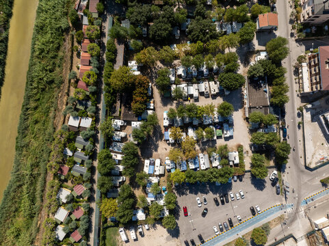 Aerial view of a campsite with numerous caravans and motorhomes nestled among trees, adjacent to a river and a parking lot in Porto San Giorgio, Marche, Italy.