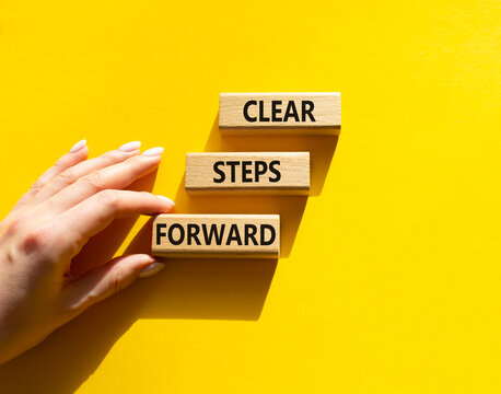Concept words clear steps forward on wooden blocks arranged as steps. Businessman hand arranging wooden blocks. Progress and planning concept. Yellow background. Copy space.