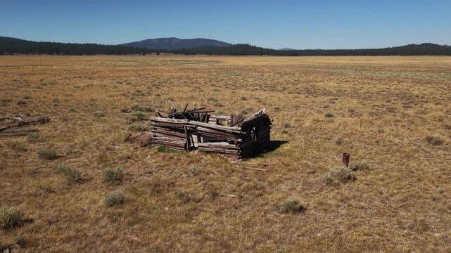 Drone close-orbits abandoned log cabin to reveal run-down corral on open rangeland, Lassen County, California.
