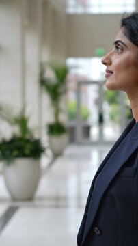 Vertical video: Responding to suit, woman in blazer reaching left, pausing and looking up in lobby