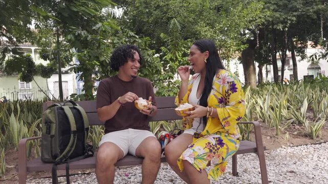 Young couple eating traditional food on park bench