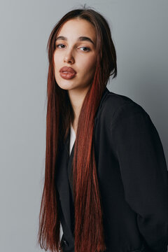 Young woman with long straight hair and natural makeup posing in black blazer against gray background. Fashion portrait with serious expression and casual style for beauty and lifestyle.