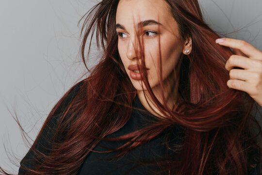 Woman with long hair in black sweater looking sideways with loose strands of hair on face. Portrait of young female with natural makeup and earrings on neutral background.
