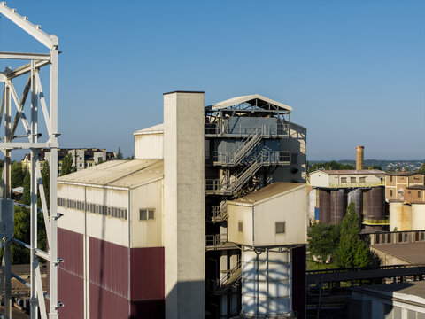 Aerial view of the cementownia industrial plant featuring tall silos, metal framework, and storage buildings under a clear blue sky in Poland.