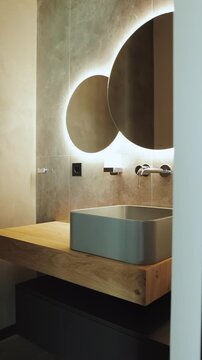 Vertical video. Modern bathroom interior with a vessel sink, wood vanity and illuminated mirror.