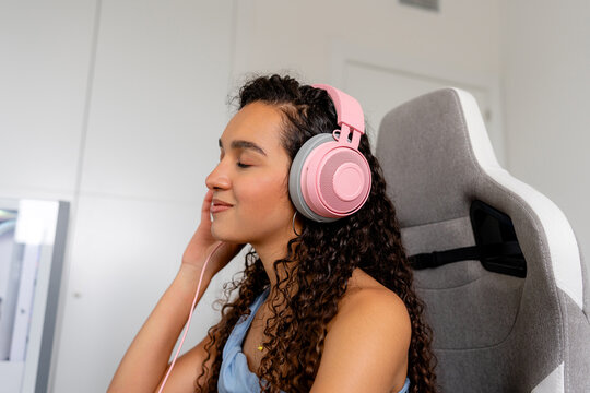 Young woman relaxes with pink headphones in gaming chair