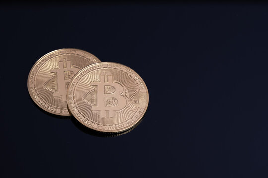 Two bitcoin coins placed on a black surface with shadows.