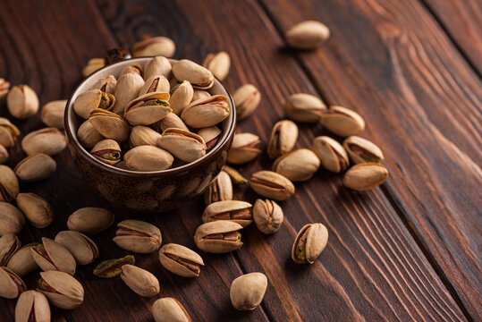 Natural healthy pistachios in bowl and scattered on wooden table background close up nutritious snack food