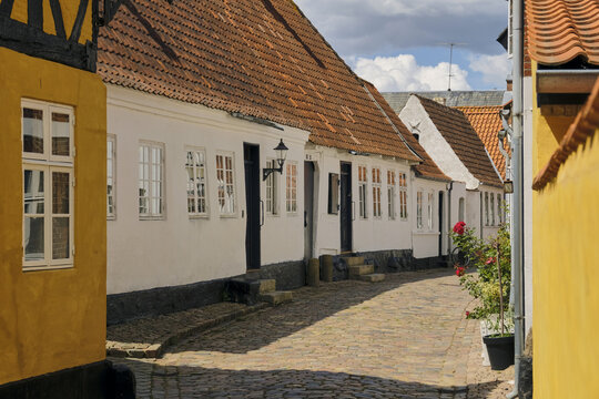 View of a charming cobblestone street lined with traditional white half-timbered houses and orange tiled roofs in the historic city of Ribe, Denmark.