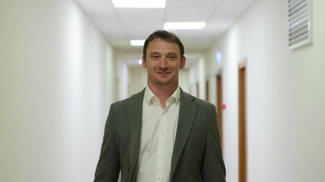 Successful male executive in a formal suit walking through a bright corporate hallway directly towards the camera.Split screen or sequence of a professional businessman walking back and forth in a con